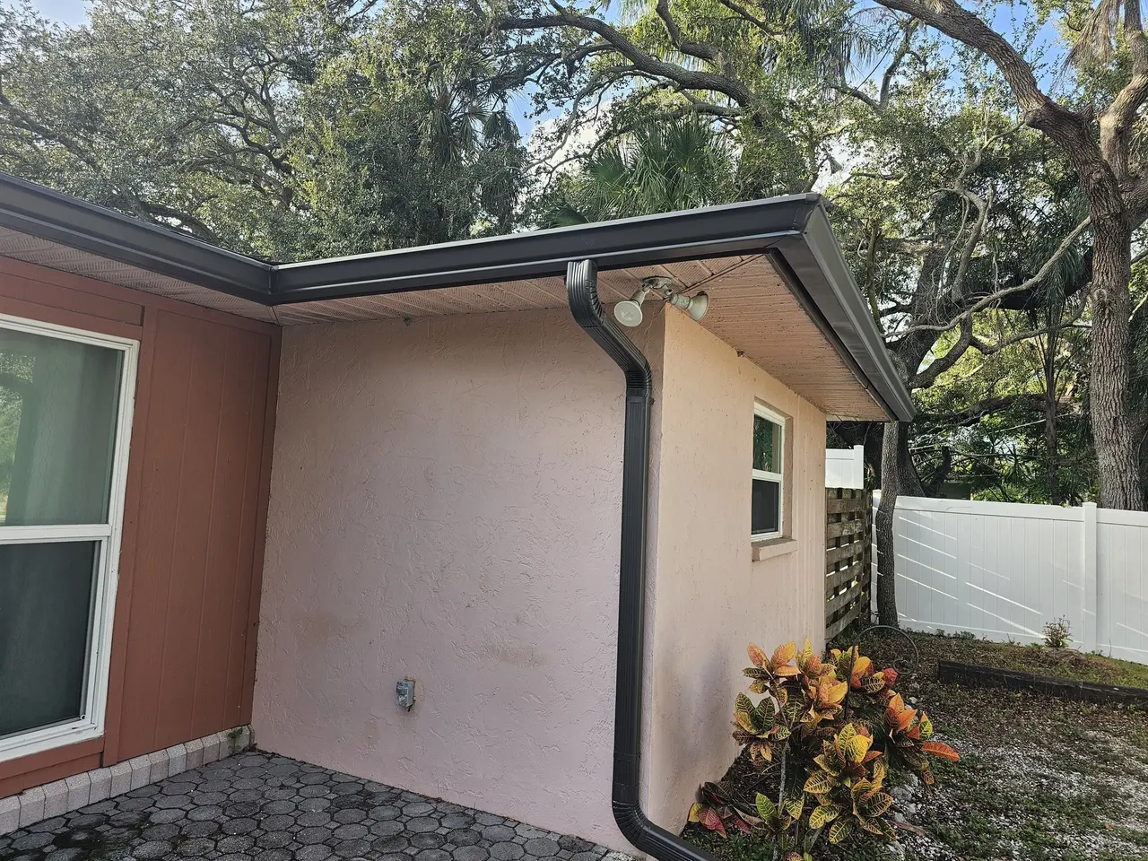 Bronze gutter and downspout on a stucco corner with a paver patio
