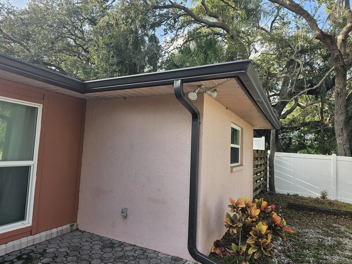 Bronze gutter and downspout on a stucco corner with a paver patio