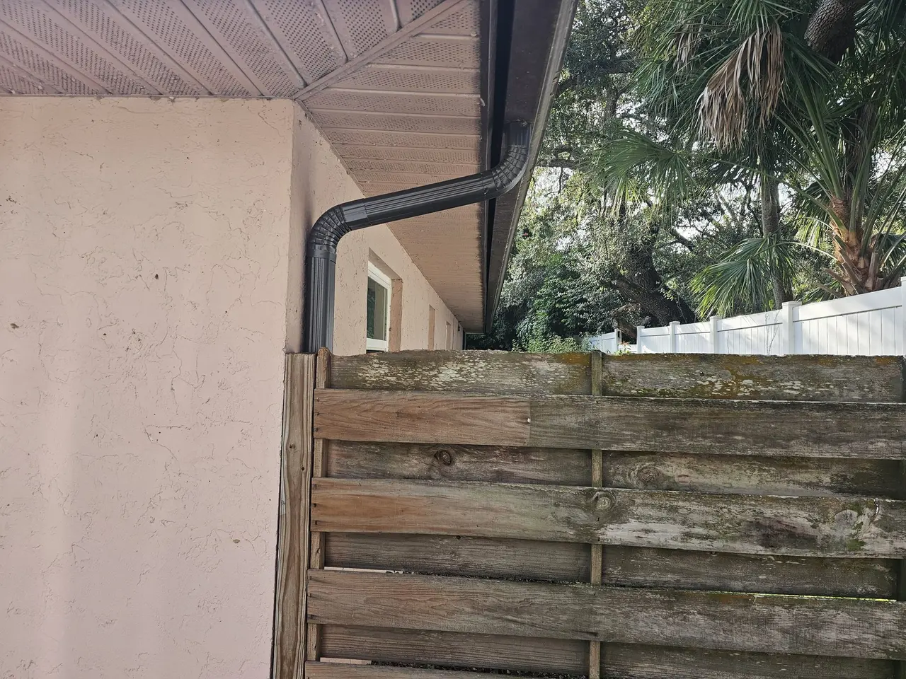 Bronze downspout on stucco beside a wood fence