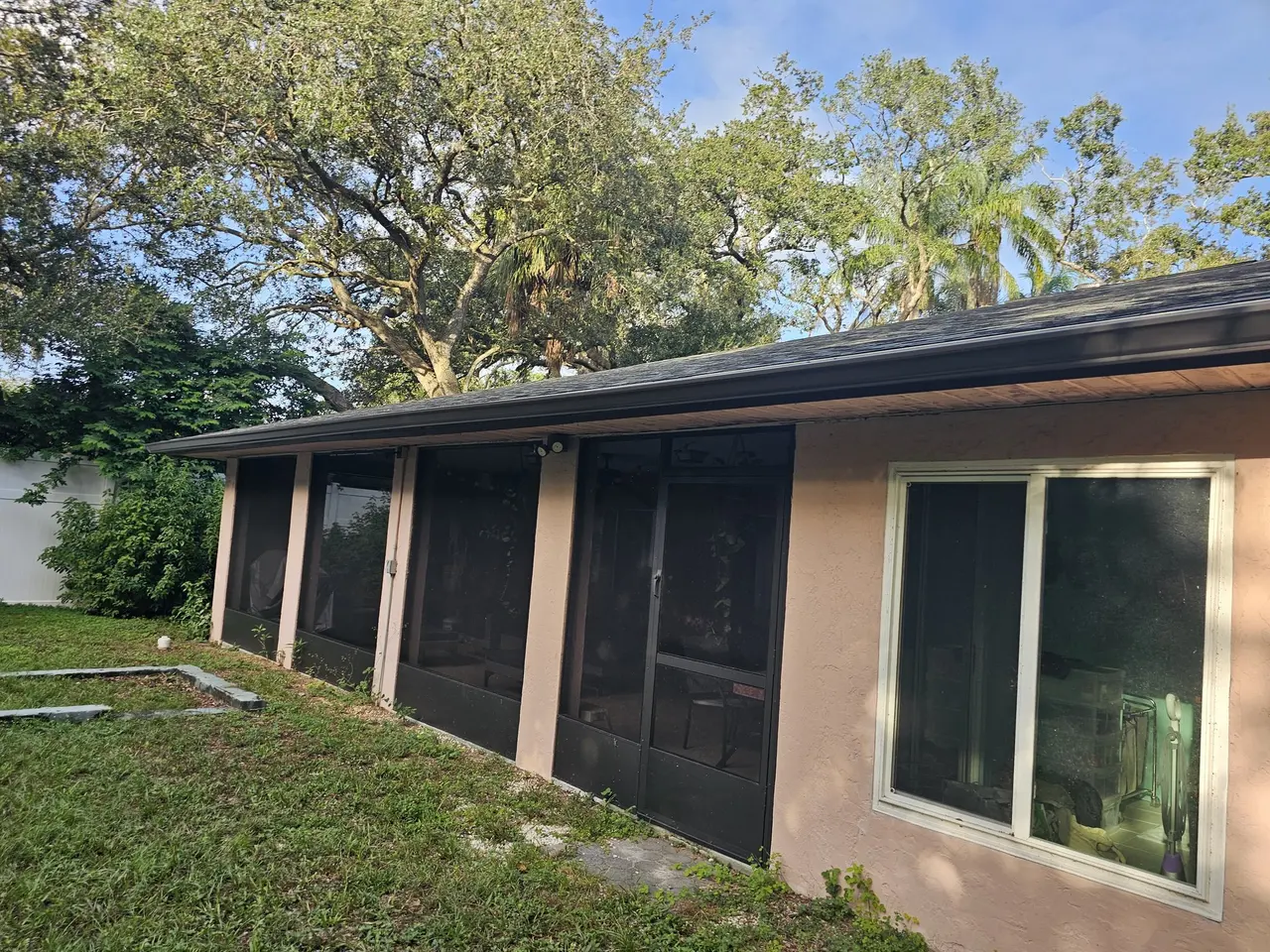 Rear of a stucco home with new bronze gutters and a screened porch