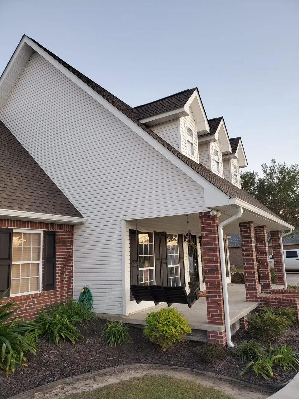 Dormered colonial corner with new white gutters and a brick porch