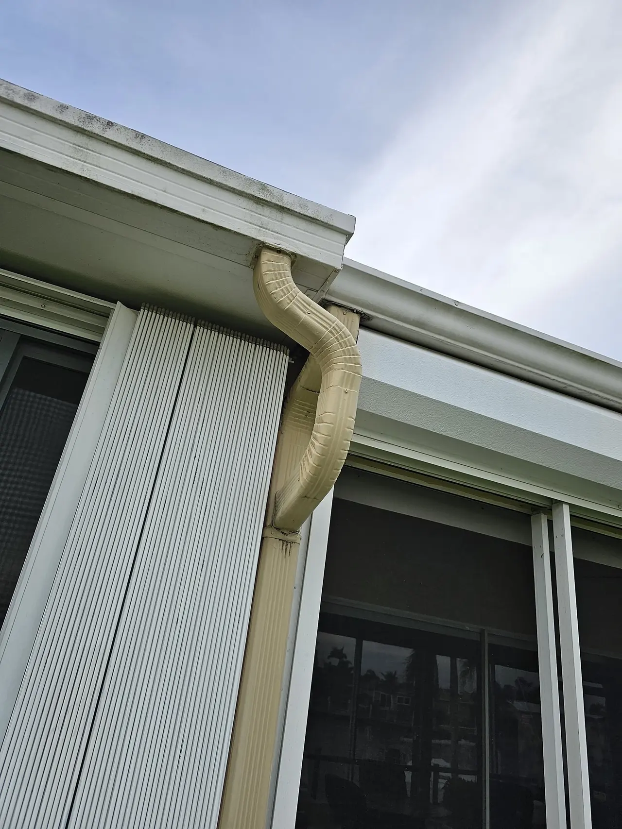 Close-up of a white gutter corner and downspout elbow on stucco