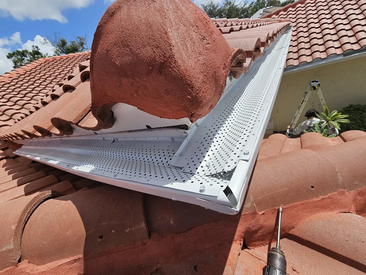 Perforated aluminum gutter guard installed under a tile roof
