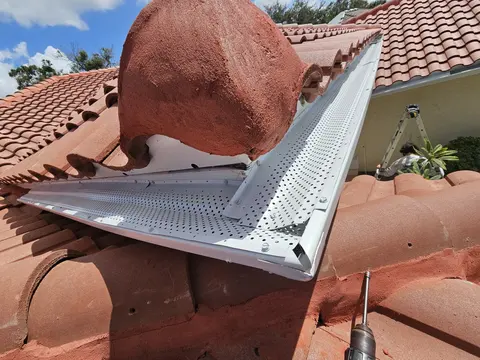 Perforated aluminum gutter guard installed under a tile roof