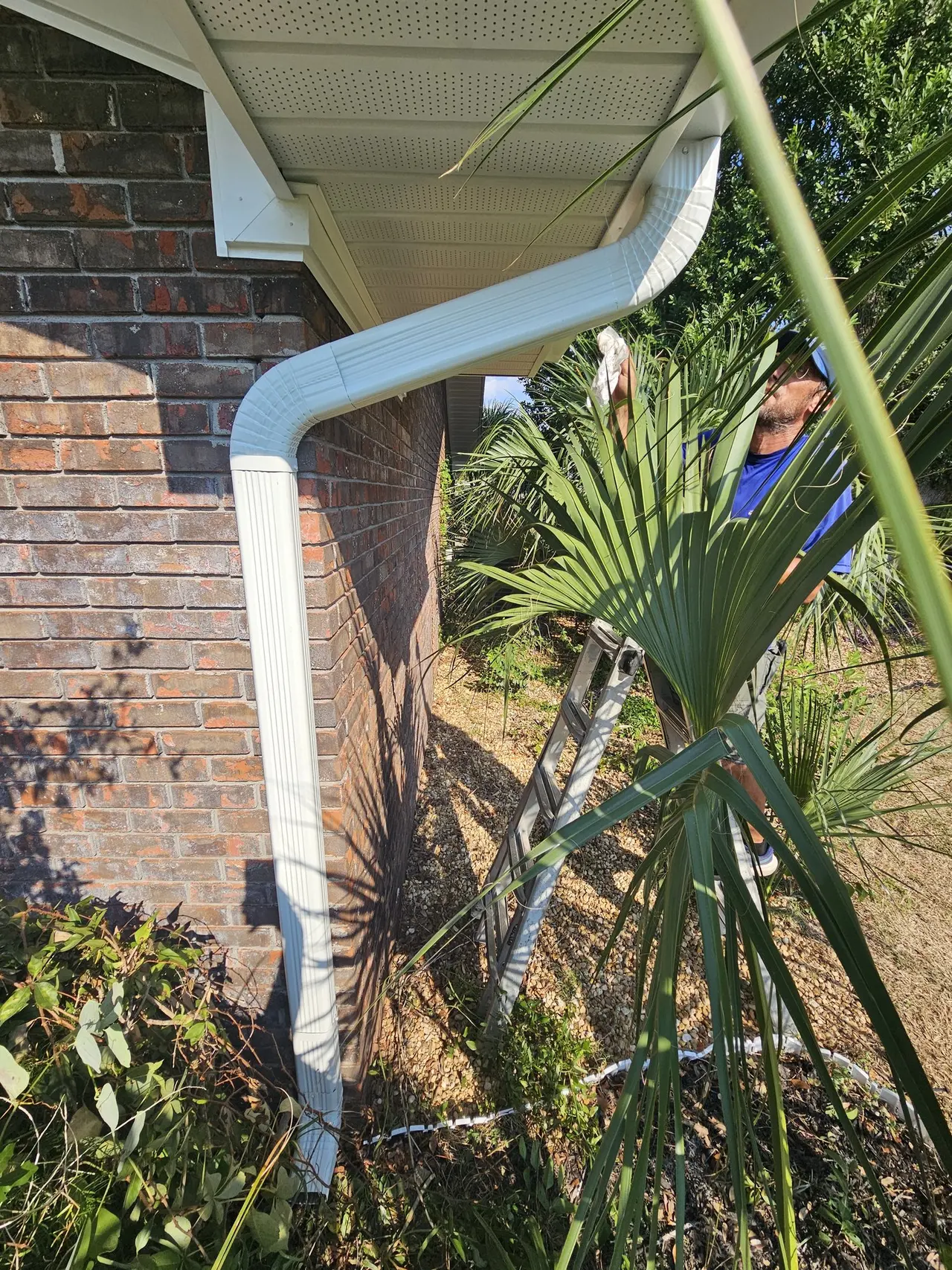 Installer on a ladder fitting a downspout on a brick wall