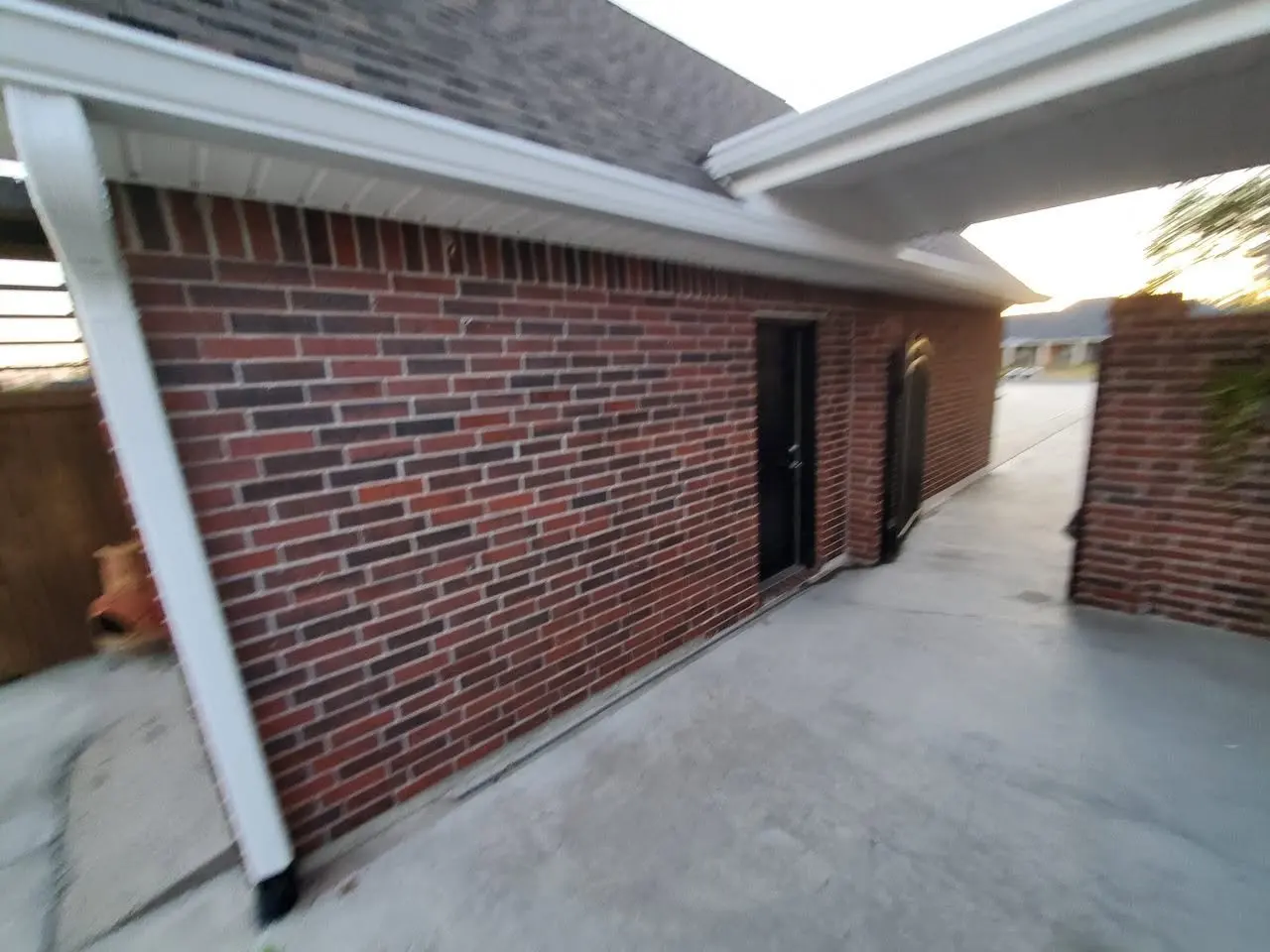 White downspout on the corner of a brick home by the driveway