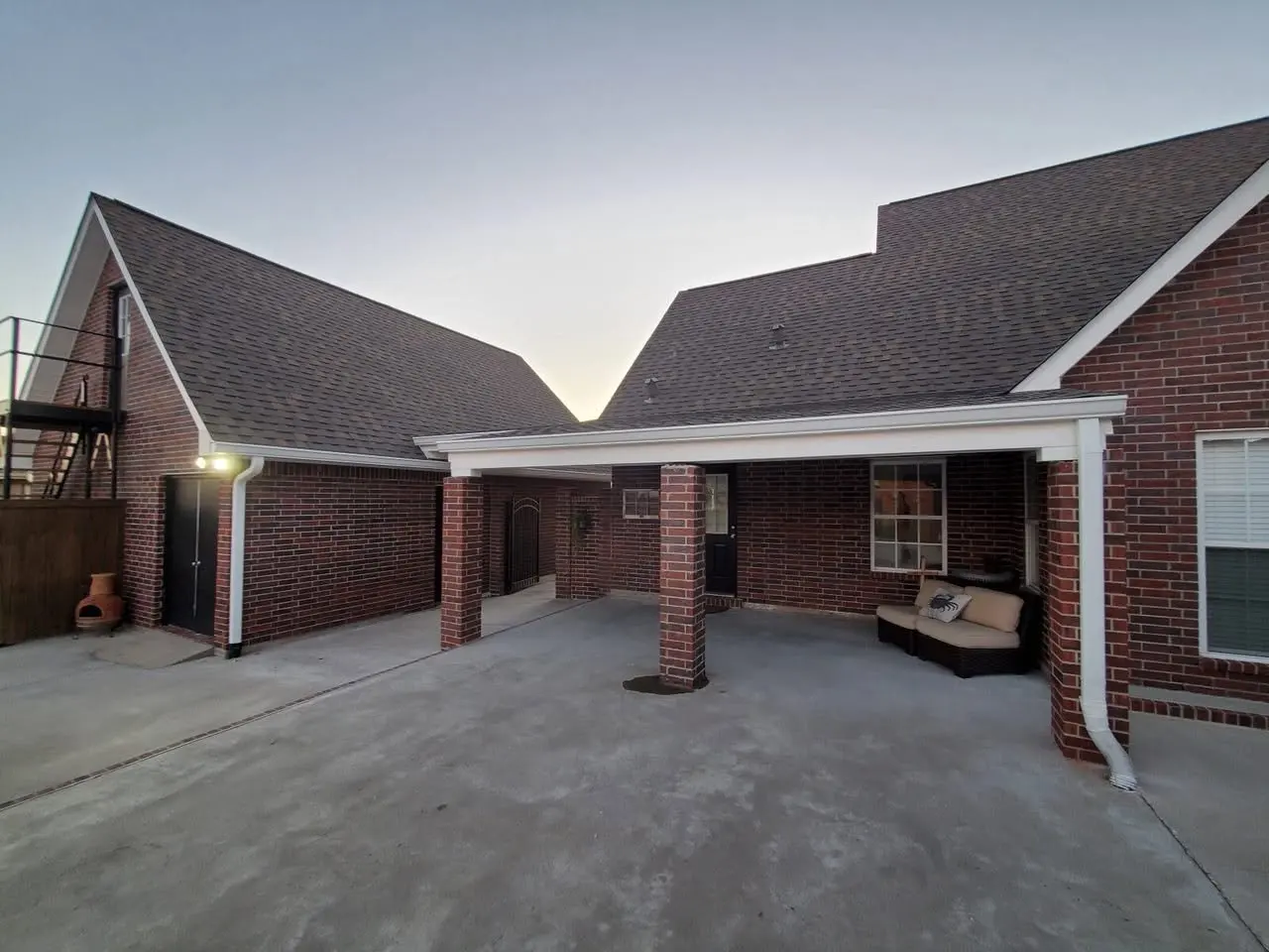 Brick home with a covered patio and white gutters at dusk