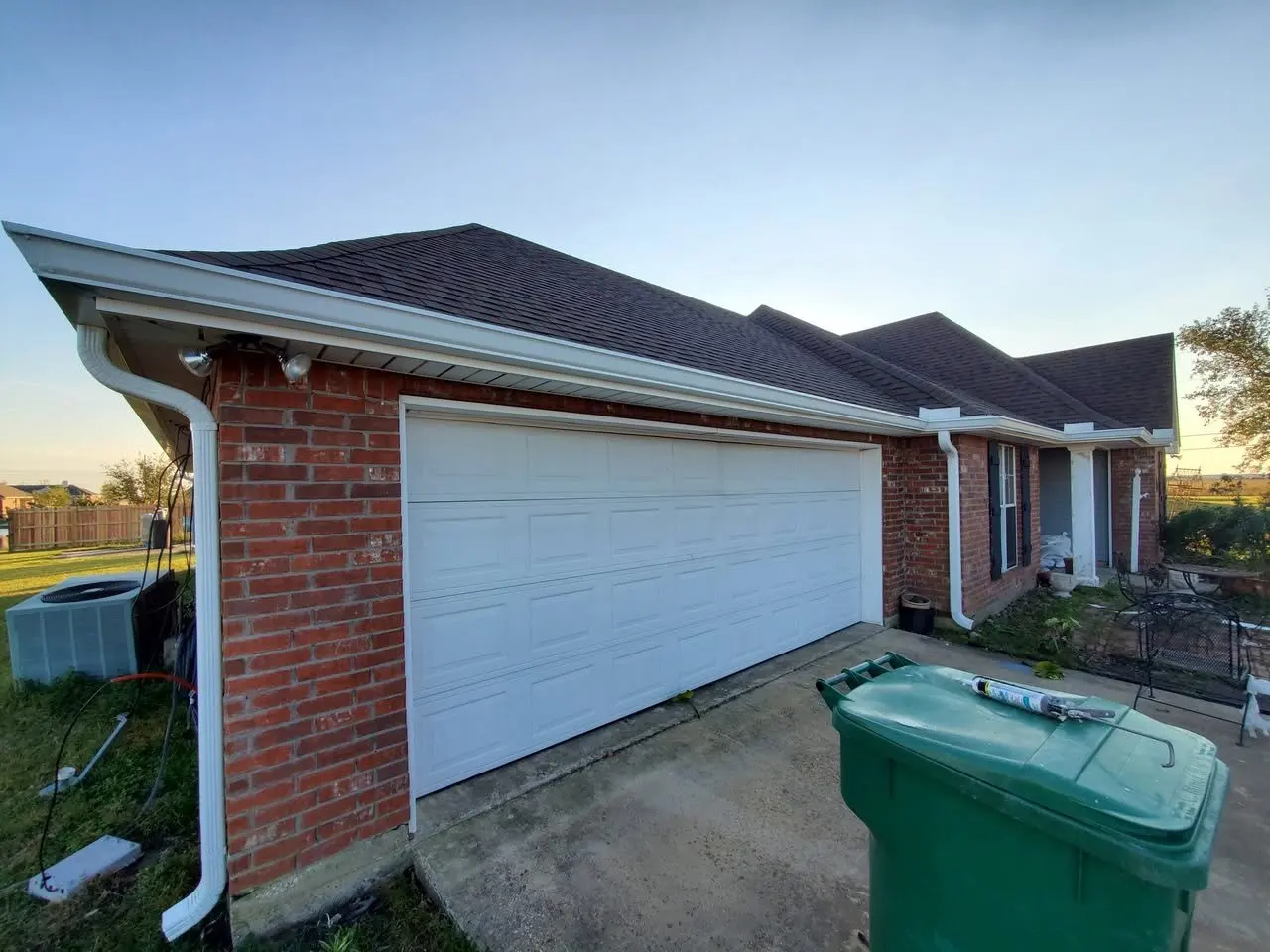 White gutter and downspout above the garage of a brick home