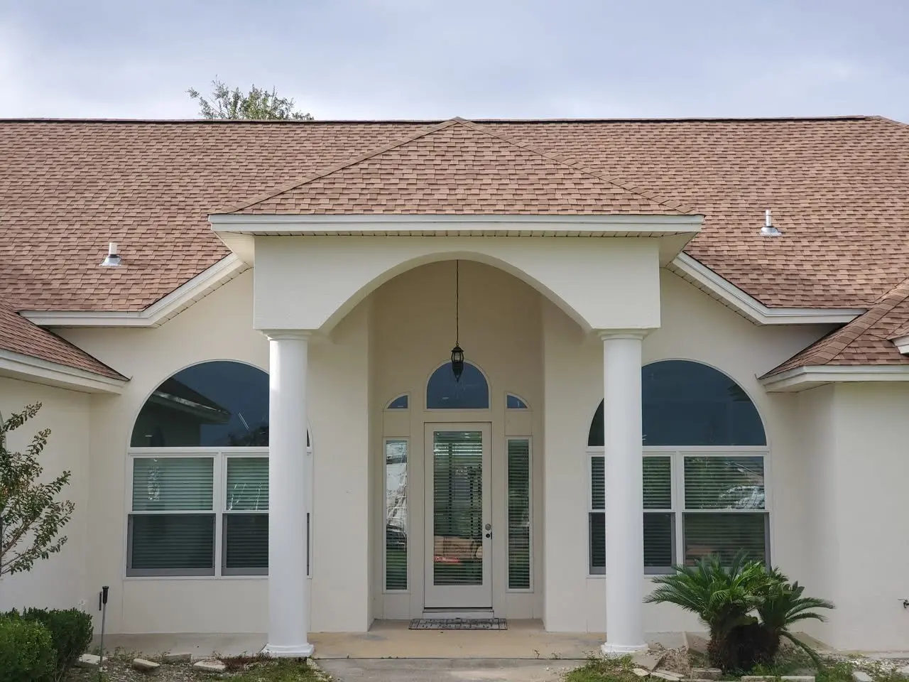 Front of a stucco home with an arched entry, columns, and white gutters