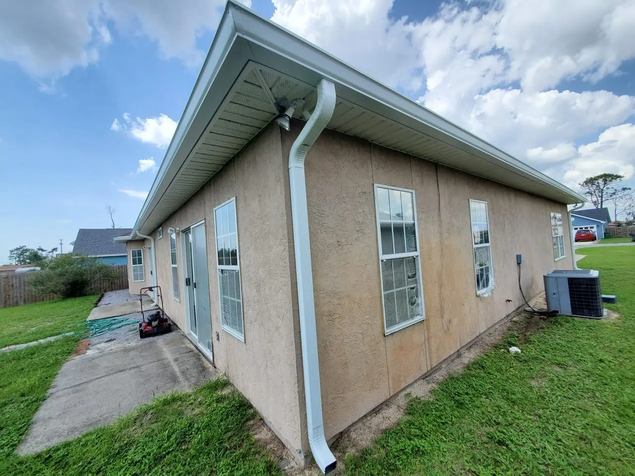Side of a stucco home with a white gutter and downspout by the AC unit