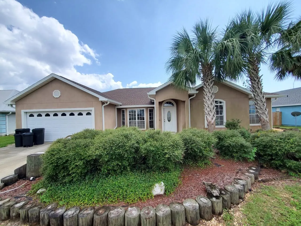 Front of a stucco home with palms, a garden bed, and new white gutters