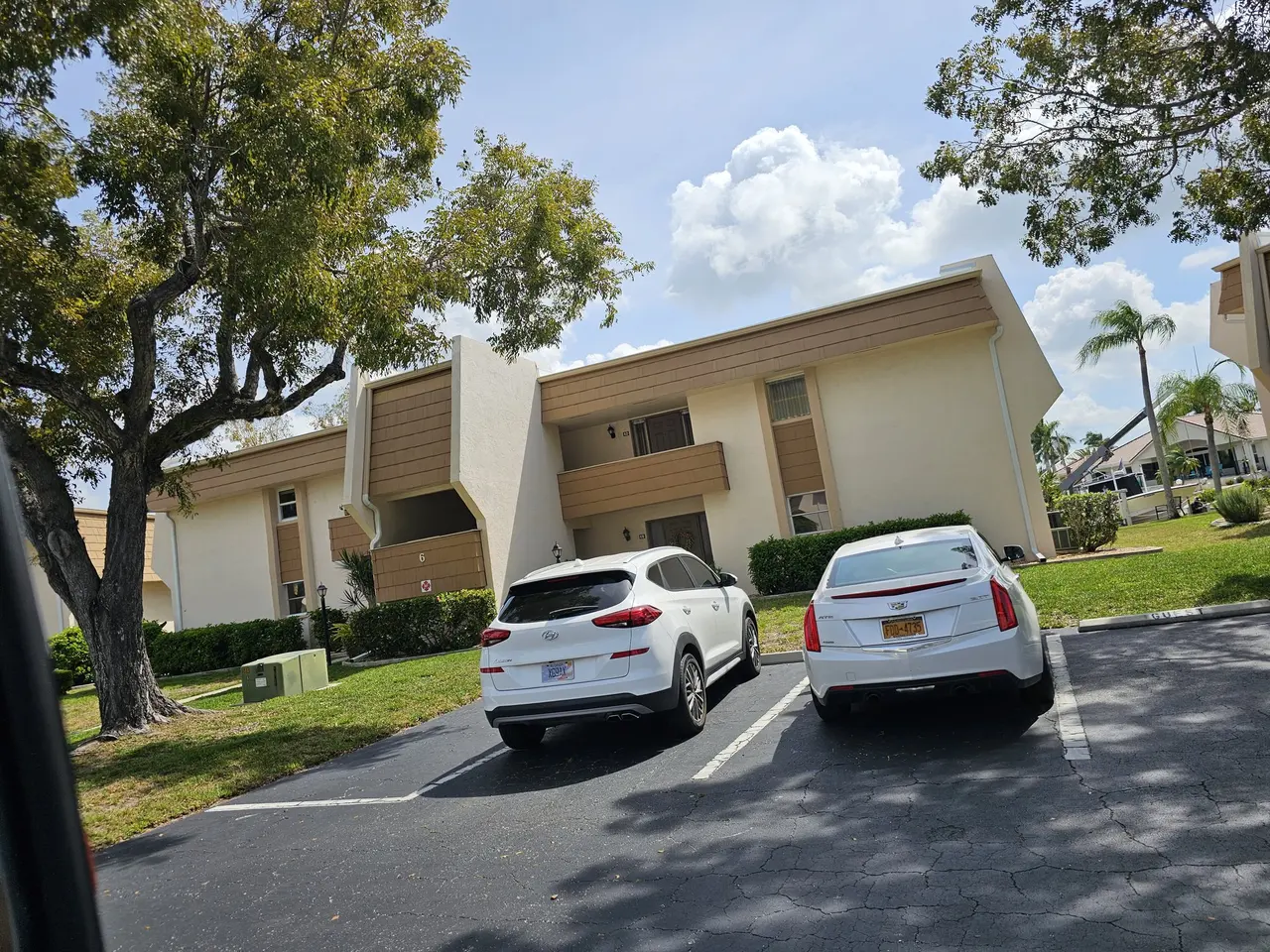 Tan stucco condo with new gutters and parked cars in front