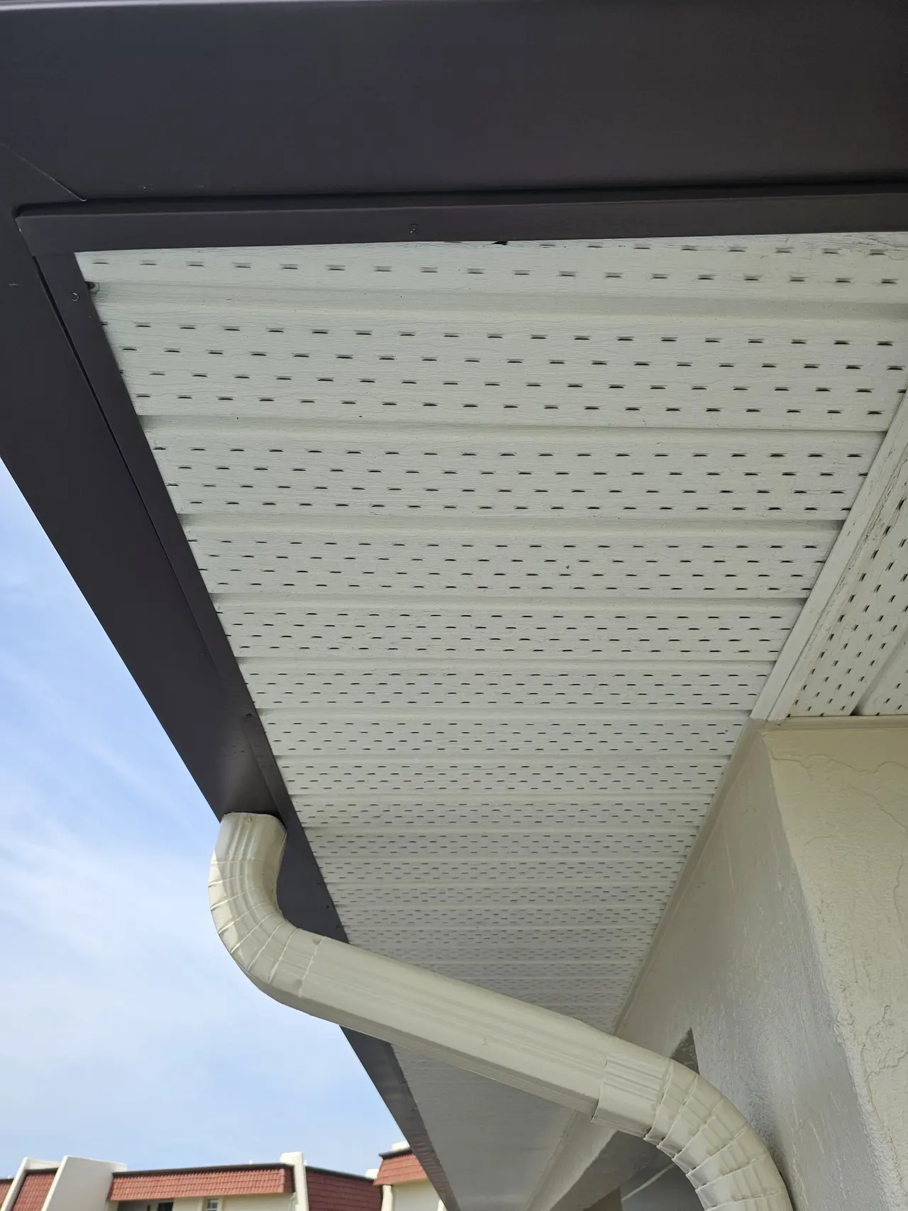 Close-up of a brown seamless gutter and downspout under a white soffit