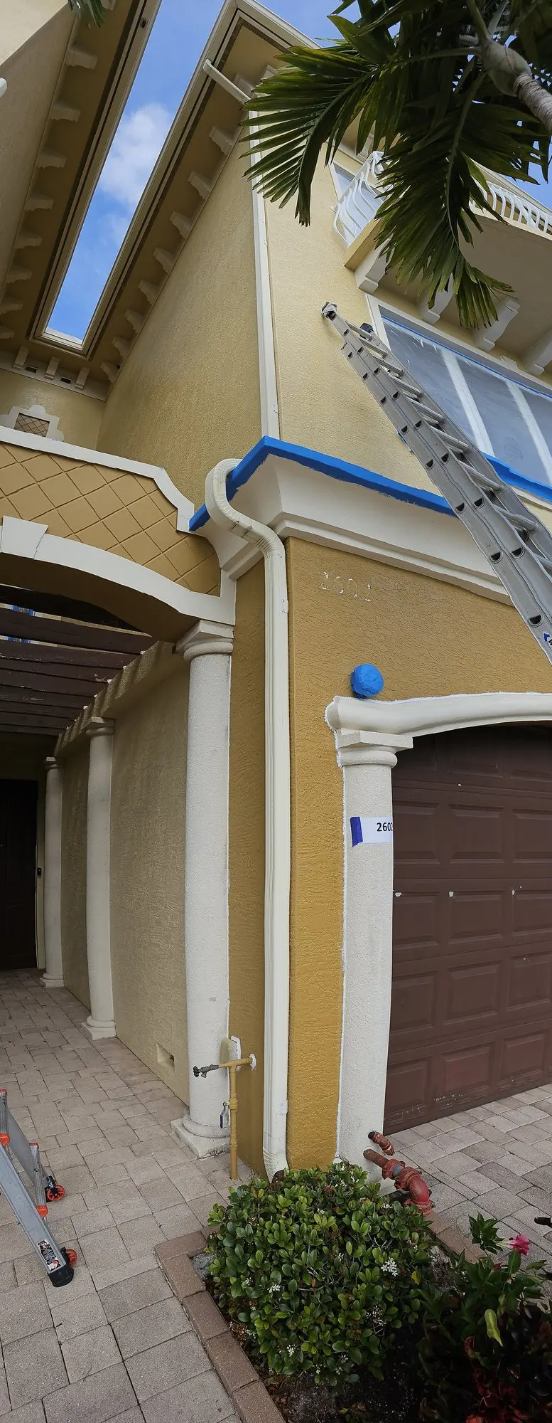 White downspout on the corner of a yellow two-story townhome with a paver driveway