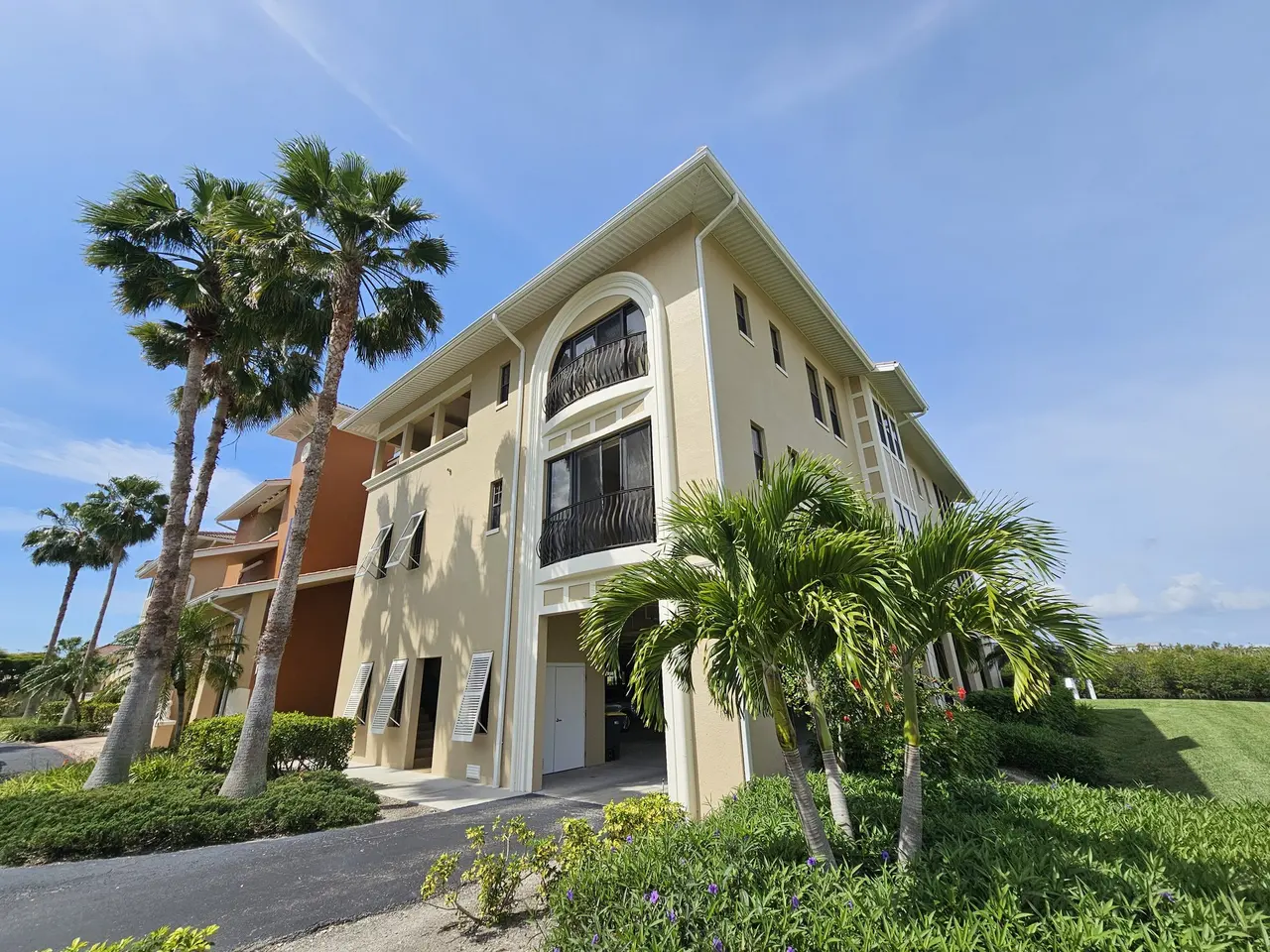 Three-story building with white gutters and a corner downspout under tall palms