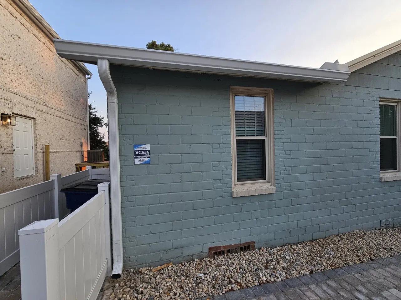 Side of a new home with white gutter and downspout, golden hour