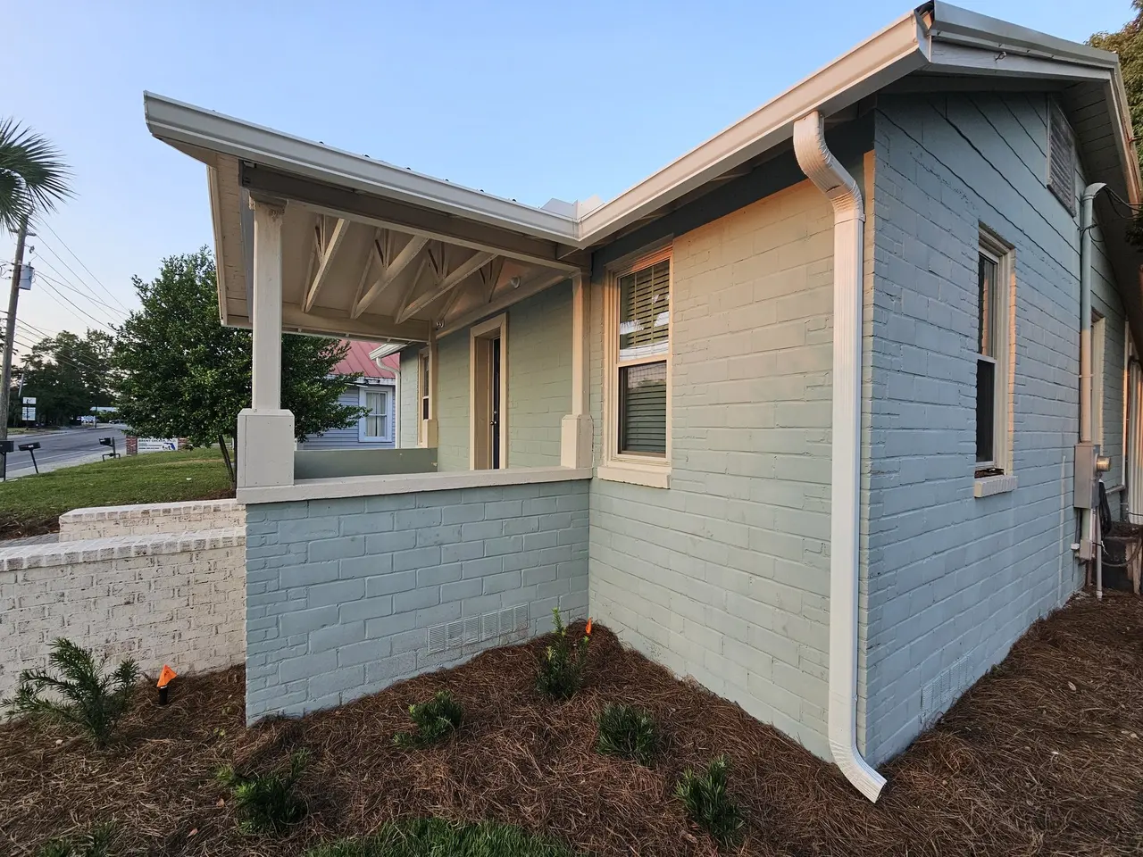 Corner of a new sage-green home with white seamless gutters at golden hour