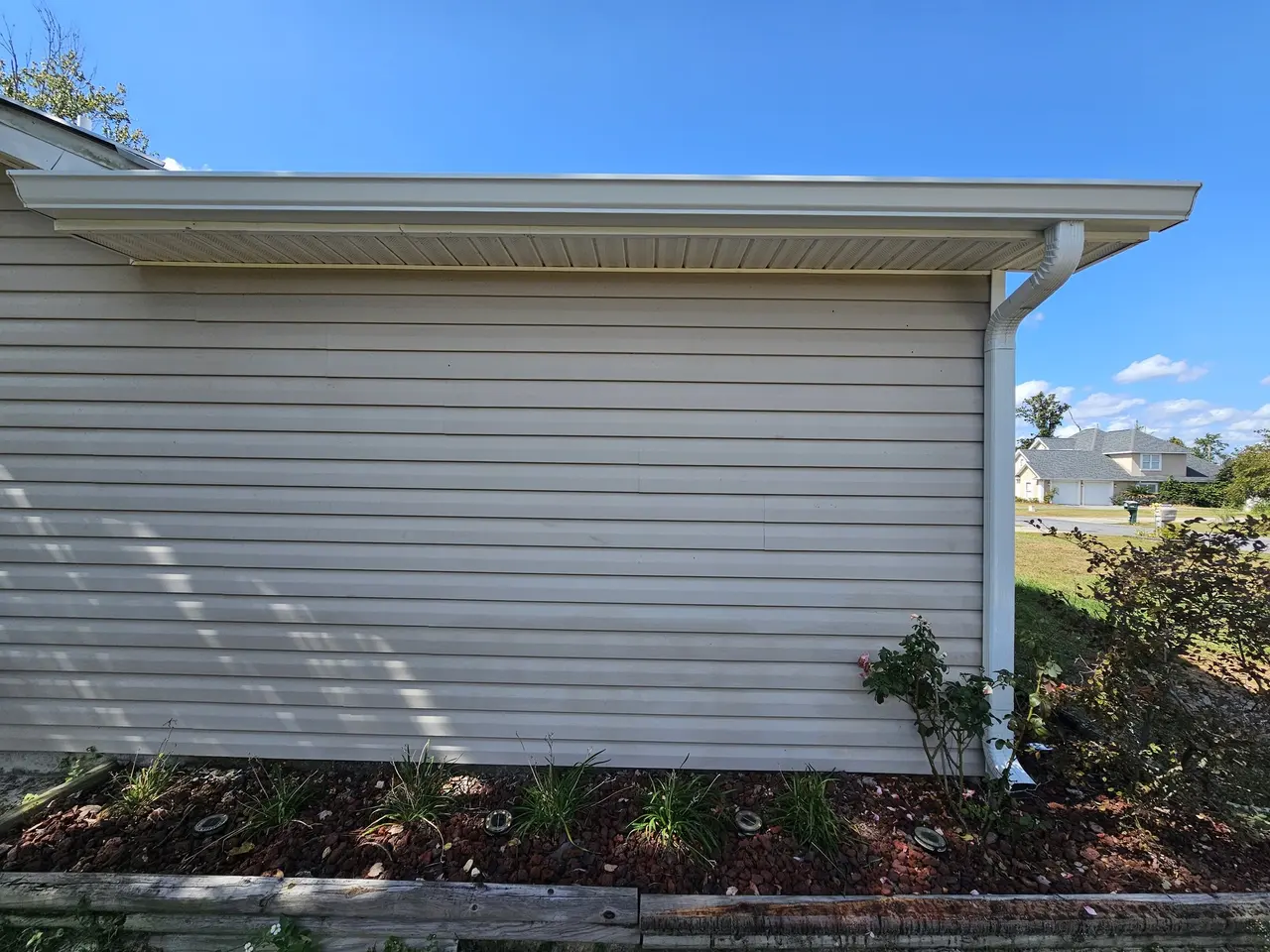 Tan vinyl-siding home with a white gutter and downspout
