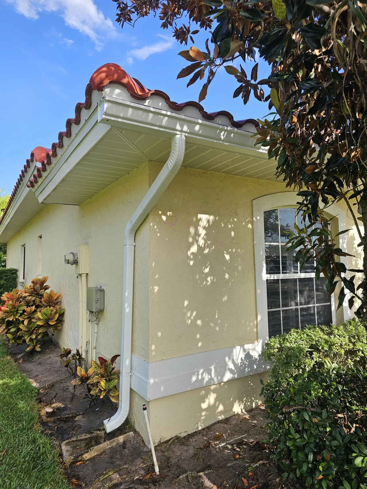 Yellow stucco home with a tile roof and white gutter and downspout