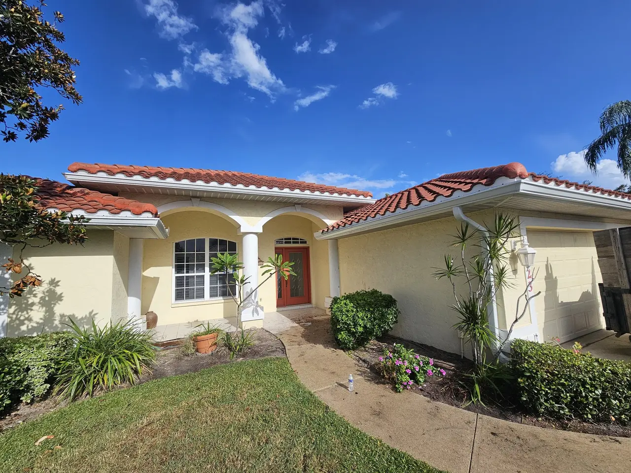 Mediterranean home with tile roof, arched entry, and white seamless gutters
